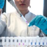 Scientist wearing blue gloves pipettes liquid into a laboratory tube. Illustrative laboratory photograph.