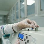A gloved laboratory analyst adjusts a small sample holder on a benchtop instrument.